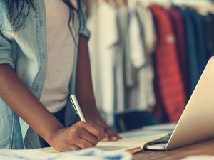 Jeune femme devant un ordinateur, prenant des notes. Cette image représente le programme Gestion de commerce.