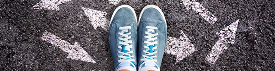 Vue en plongée de souliers bleu sur l'asphalte avec des dessins de flèches blanches qui pointes de différents côtés.