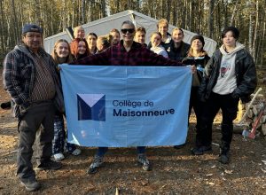 Groupe d'étudiantes et d'étudiants posant devant la tente avec Nancy Moreau, enseignante, qui tient le drapeau du Collège de Maisonneuve.